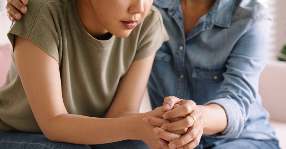 Mental health services in action: picture of an older woman holding the hand of a distressed teen girl.