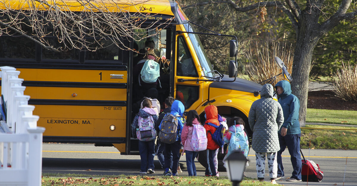 Children board school bus as parents wait on curb